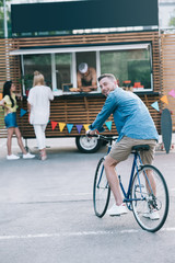handsome man sitting on bike near food truck and looking at camera
