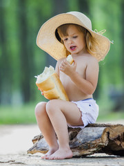 Young beautiful toddler girl sitting on a wooden log eating bread