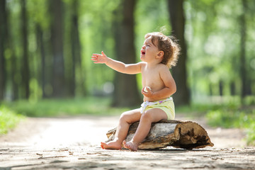 Young beautiful toddler girl sitting on a wooden log crying