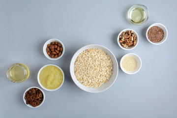 Ingredients for cooking homemade granola: oatmeal, applesauce, honey, oil, almond, walnut, raisin, flax and sesame seeds on wooden gray background. Flat lay. Top view.