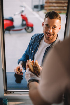 cropped image of chef giving tasty hot dog to handsome customer in food truck