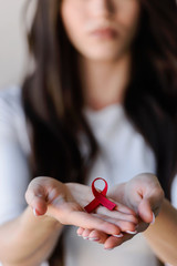 Woman holding red ribbon on her palms. AIDS awareness symbol - obrazy, fototapety, plakaty
