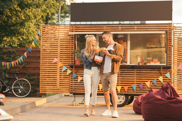 smiling couple holding french fries and burger near food truck