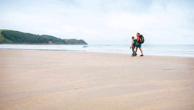 Mother and son walks together on sandy beach on the famous Camino del Norte Way, Spain