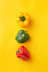 Variation of different color bell peppers on a yellow background. Colorful paprikas viewed from above isolated on yellow. Top view