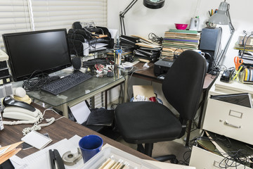 Messy business office desk with piles of files and disorganized clutter.