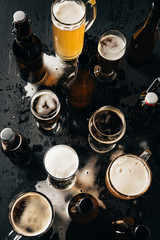 top view of arrangement of bottles and glasses of beer on dark wooden tabletop