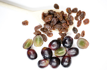raisins on a wooden spoon on white background with grapes