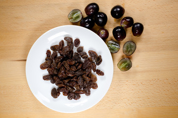 raisins on white plate with grapes on wooden background