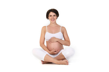 Junge schwangere Frau sitzt im Schneidersitz und hält sich lächelnd den Bauch
