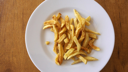 A plate of fried potatoes rotates against the background of a wooden table. Potato - chips, as a side dish for a meat dish for lunch.