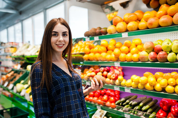 Shopping woman looking at the shelves in the supermarket.  Portrait of a young girl in a market store at fruits and vegetables section.
