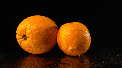 Ripe oranges on a mirror background. A fresh orange rotates on a wet mirror.