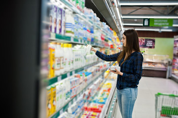 Shopping woman looking at the shelves in the supermarket.  Portrait of a young girl in a market store holding milk production.