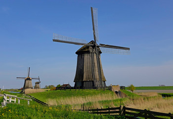 Fototapeta na wymiar Beautiful view of wooden windmills near small canal running through countryside.