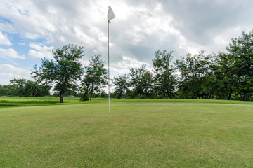 Obraz premium White Flag on a hole in Golf course. Beautiful landscape of a golf court with green trees and blue sky clouds.