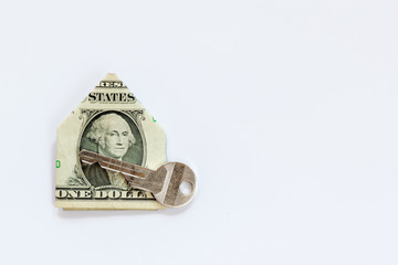 Mortgage concept: one dollar bill folded as a house with a key on top on a light grey background