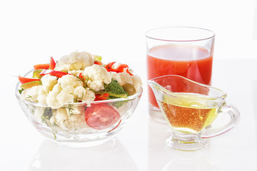 Fresh salad of cauliflower with tomato, broccoli, olives, sweet pepper, greens with a glass of tomato juice and a glass nipple on a white background