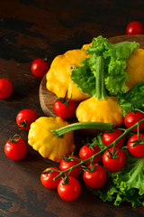 organic yellow patissons with cherry tomatoes and salad on a wooden table. a new harvest of vegetables from the garden, vegan food, a diet food. selective focus and copy space
