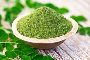 Moringa powder in coconut bowl with original fresh Moringa leaves on wooden background