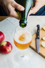 Close-up image of man pouring premium cidre in glass. Top view of male hands pouring vintage apple wine into beautiful glass in rustic table background with ripe apples
