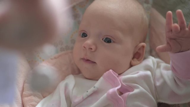 Slow motion shot of quiet two months baby girl is attracted with crib toys hanging above