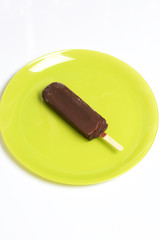 Ice cream ice in chocolate on a stick. Lies on a plate of light green color. White background.