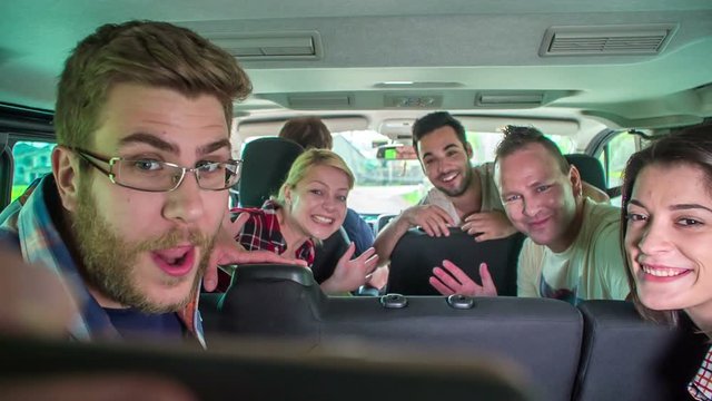 A group of friends is taking a photo together in a van while a driver is driving.