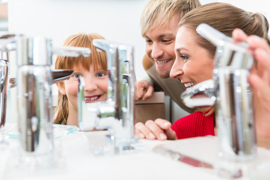 Low-angle Portrait Of A Happy Family, Looking For A New Bathroom Sink Faucet In A Modern Sanitary Ware Shop With High-quality Fixtures And Appliances