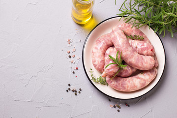 Fresh homemade raw sausages on plate on grey textured background.