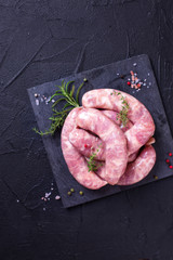 Raw homemade sausages os slate board on black textured background.