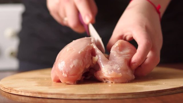 Female chef cuts raw chicken meat on a round wooden Board. High resolution. The view from the top. Cook chef hands woman cuts raw meat chicken breast on a wooden background