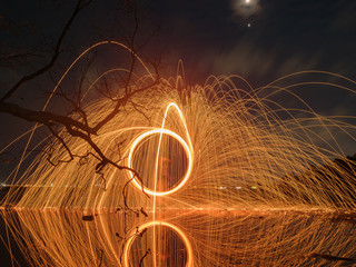 light lines of steel wool with long exposure, speed motion abstract background in the dark night with dry branch tree and reflection in water