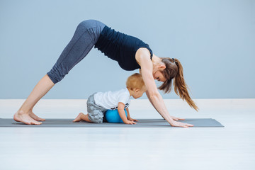 Beautiful mother and little toddler son practicing yoga together at home, making back stretching exercise, standing in dog pose, copy space