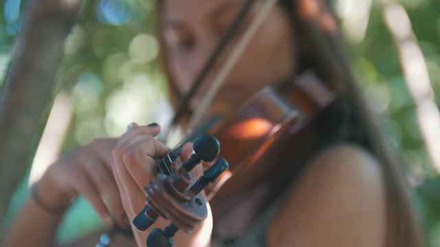Young woman playing a violin standing on the grass in the park at sunset