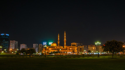 Fototapeta na wymiar King Faisal mosque at nigh,the biggest mosque in Sharjah . People are resting near mosque in a park.