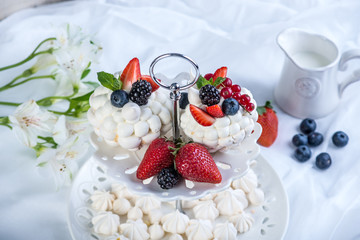 Delicate white meringues with fresh berries on the plate on white background. Dessert Pavlova. Wedding cake.