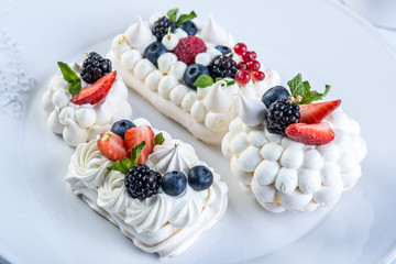 Delicate white meringues with fresh berries on the plate on white background. Dessert Pavlova close-up. Wedding cake.