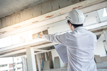 Asian male engineer or architect checking blueprints or architectural drawing while wearing protective safety helmet at construction site. Engineering, Architecture and building construction concepts