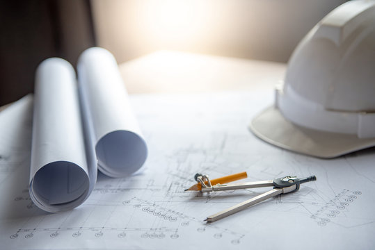 Compass tool and safety helmet on architectural drawing plan of house project, blueprint rolls on working table, Architecture and building construction industry concepts
