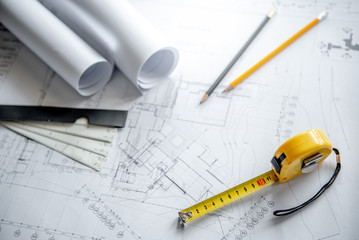 Yellow tape measure (measuring tape), scale and pencils on architectural drawing plan of house project, blueprint rolls on working table, Architecture drawing tools and building construction concepts