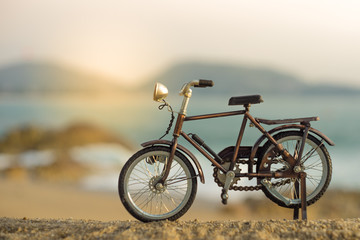 Obraz premium bicycle transport toy on sand sea beach in the evening sunset sky , with yellow light beam