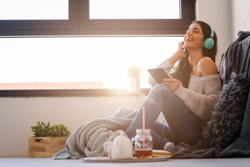 Beautiful young woman at home enjoys listening music through headphones