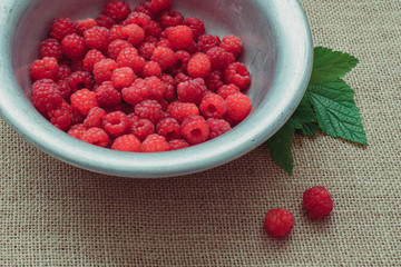 Rustic still life of ripe raspberries with a leaf in a rustic aluminum plate on the background of sacks, useful food and vitamins
