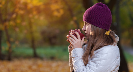 Autumn concept. Beautiful woman wearing coat and knitted hat with coffee mug standing on fall nature background