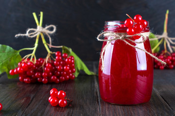 Glass jar of homemade viburnum jam with fresh berries  on dark wooden table.