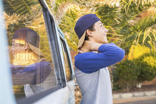 beautiful male teenager in cassual dress outdoor in leisure activity smiling and enjoying the tropical weather. mirrored in a vintage van vehicle