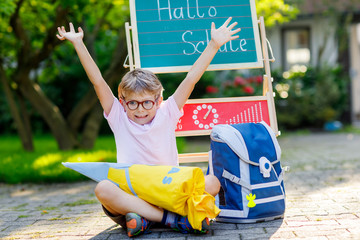 Happy little kid boy with glasses sitting by desk and backpack or satchel. Schoolkid with traditional German school bag cone called Schultuete on his first day to school