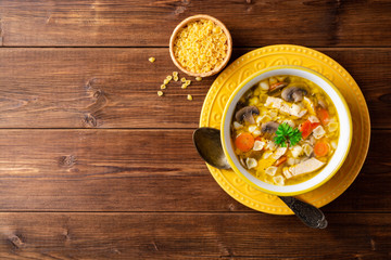 Chicken soup with mushrooms, vegetables and pasta in bowl on wooden table.