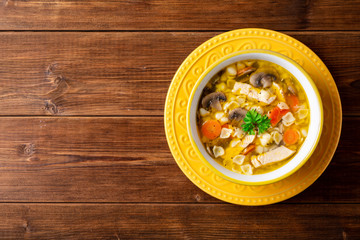 Chicken soup with mushrooms, vegetables and pasta in bowl on wooden table.